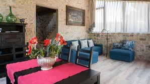 Una habitación rústica con paredes de piedra, un sofá azul, una mesa de madera con mantel rojo y un jarrón de flores rojas.