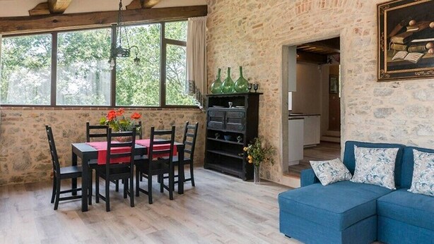 A rustic room with a stone wall, a dining table with chairs, a blue sofa, and a bookshelf.