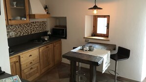 A compact kitchen with wooden cabinets, a microwave, a small window, and a bar stool.