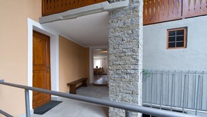 A hallway with a wooden door, a stone pillar, and a metal railing.