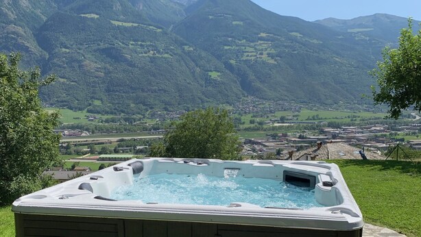 A hot tub with steps, set on a stone patio with a mountain view.