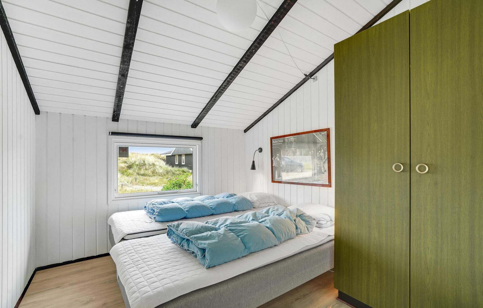Um quarto com uma cama, janela, guarda-roupa e um quadro na parede.
