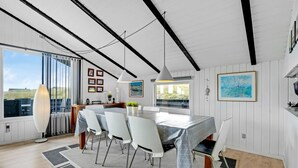 A modern dining area with a large table, white chairs, and a view of the outdoors.