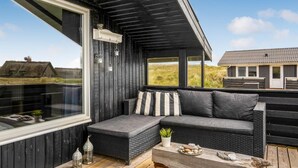 A cozy outdoor seating area with a dark wooden bench, a cushioned sofa, and a small table with a plant and stones.