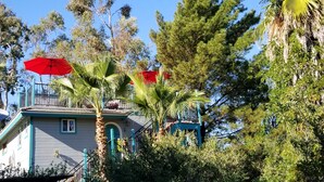 A building with a balcony, surrounded by trees and a red umbrella.