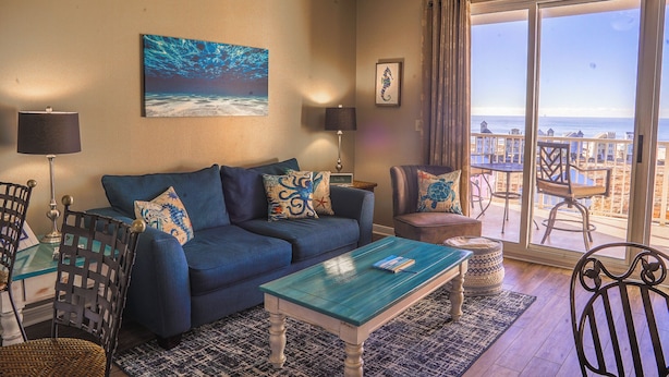 A living room with a blue sofa, a coffee table, and a view of the ocean through a large sliding glass door.