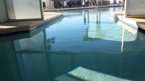 A clear swimming pool with a tiled edge, a pool ladder, and lounge chairs in the background.