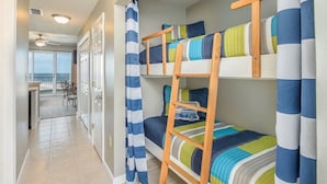 A room with bunk beds, a ladder, a curtain, and a view of the balcony.