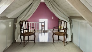 A room with a sloped ceiling, two wooden chairs, a large hanging light fixture, and a view of a balcony with a railing. - Villa 6 persons, 100 m from the sea (Saint-Martin de Bréhal)