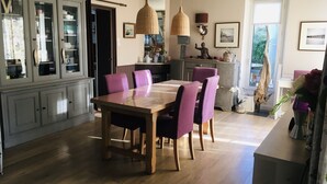 A dining area with a wooden table and purple chairs, a grey cabinet with glass doors, and a hanging woven light fixture. - Villa 6 persons, 100 m from the sea (Saint-Martin de Bréhal)