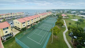 Ein Küstenhotel mit mehreren Gebäuden, einem Tennisplatz und einem Yachthafen.