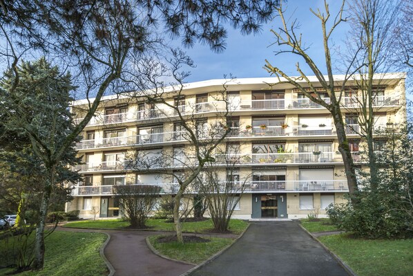Un edificio residencial de varios pisos con balcones, una entrada central y un área verde circundante.