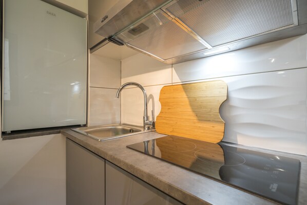 A modern kitchen with a stainless steel sink, a wooden cutting board, and a built-in oven. - Residence 3 people Paris (Fontenay-aux-Roses)