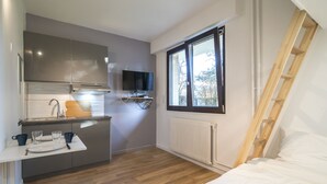 Een compacte kamer met kitchenette, een bed, een raam en een houten trap.
