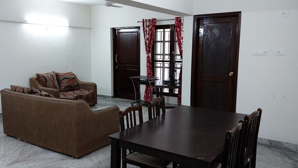 Una sala de estar con sofá, una mesa de comedor con sillas, televisión y ventana con cortinas.