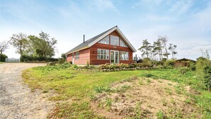 Een tweelaags houten huis met een schuin dak, grote ramen en een verzorgde tuin met een grindpad naar de ingang.