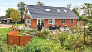 Eenlaags huis met een schuin dak, een veranda met tafel en stoelen, en een verzorgde tuin met diverse planten en een klein vijvertje.