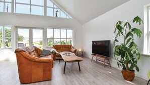Een ruime woonkamer met een groot raam, een leren bank, een houten salontafel, een televisie en een grote potplant.