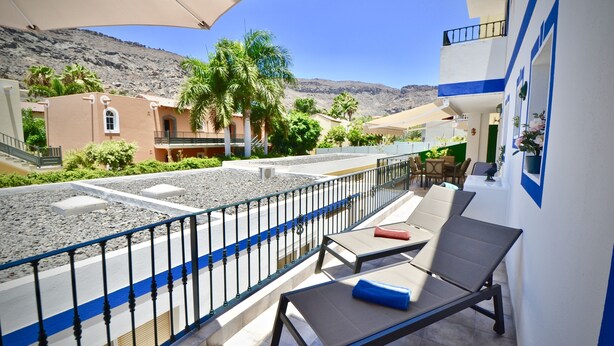 A balcony with lounge chairs, a view of a street with buildings and palm trees, and a mountainous backdrop. - Casa Bonita - Big terrace close to the beach (Lomo Quiebre)