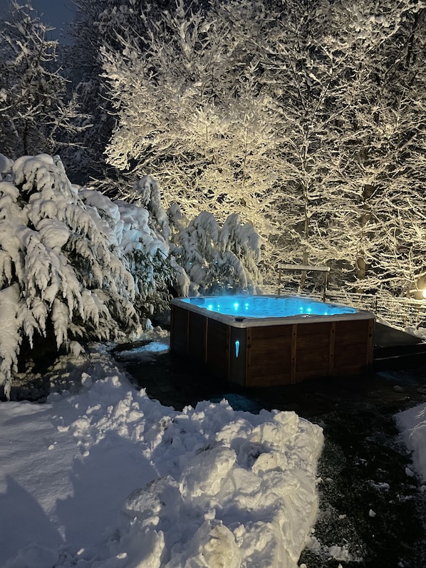 Ein hölzernes Whirlpoolbad, umgeben von schneebedeckten Bäumen und einer verschneiten Landschaft.