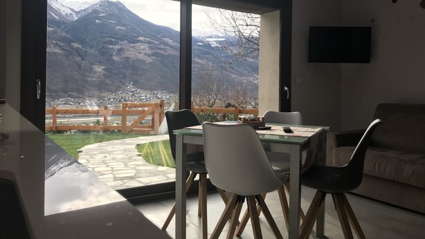 A dining area with a table and chairs, a sofa, and a TV on the wall.