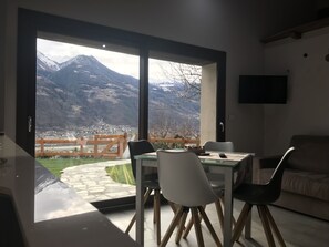A dining area with a table and chairs, a sofa, and a TV on the wall. - The Harmony Of Nature (italia)
