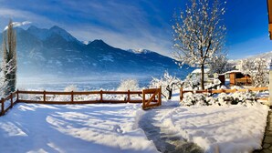 A snow-covered landscape with a wooden fence, a clear sky, and mountains in the background.
