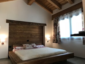 Ein Schlafzimmer mit hölzernem Kopfteil, einem Bett mit weißer Bettwäsche, zwei Wandleuchten und einem Fenster mit Vorhängen.