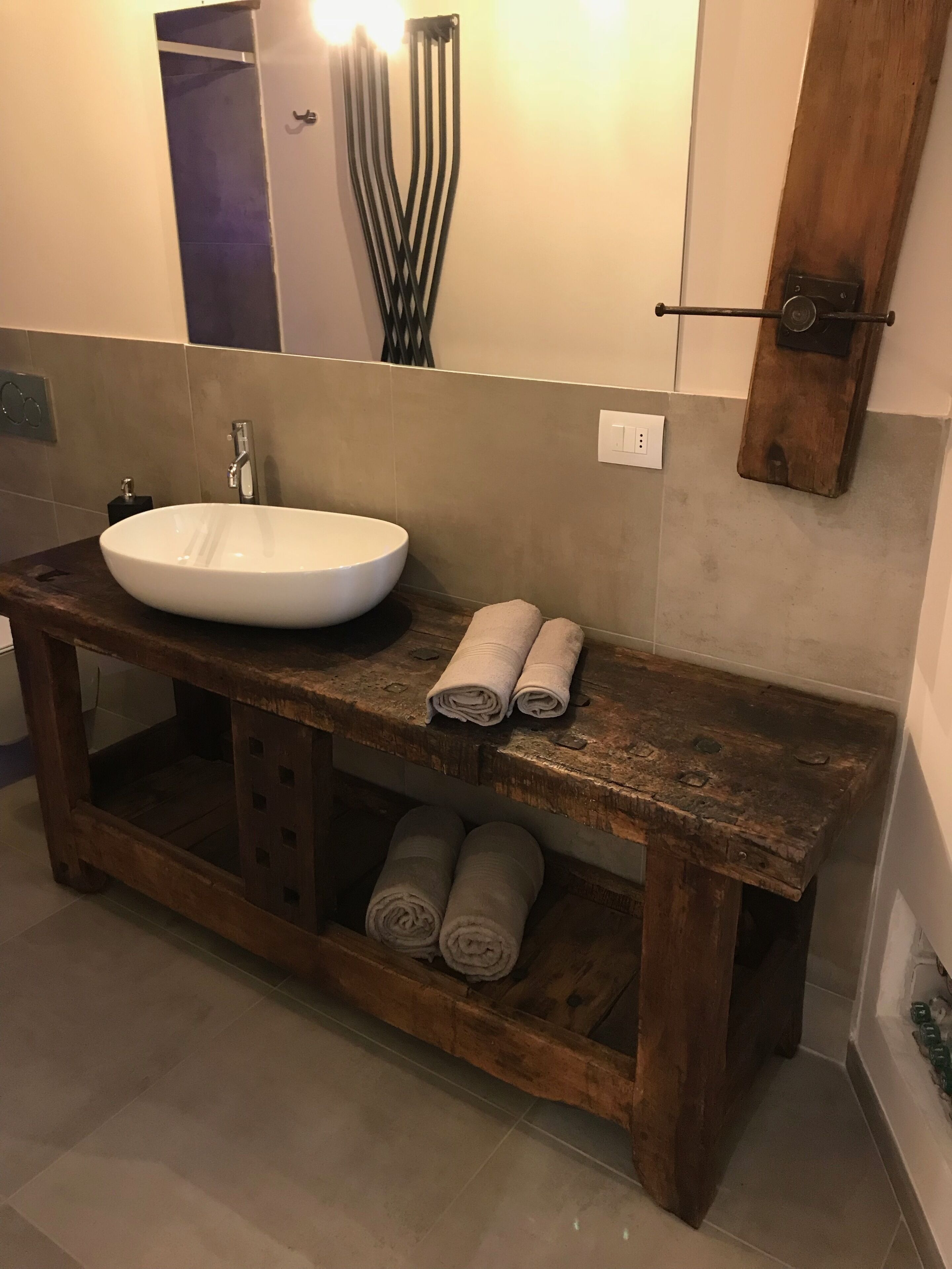 Une salle de bain avec un meuble-lavabo en bois, un lavabo blanc et deux serviettes enroulées posées sur le comptoir.