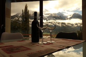 Ein Tisch mit einer Flasche, zwei Gläsern und einer Tischdecke mit Blick auf Berge, sowie ein Stuhl.