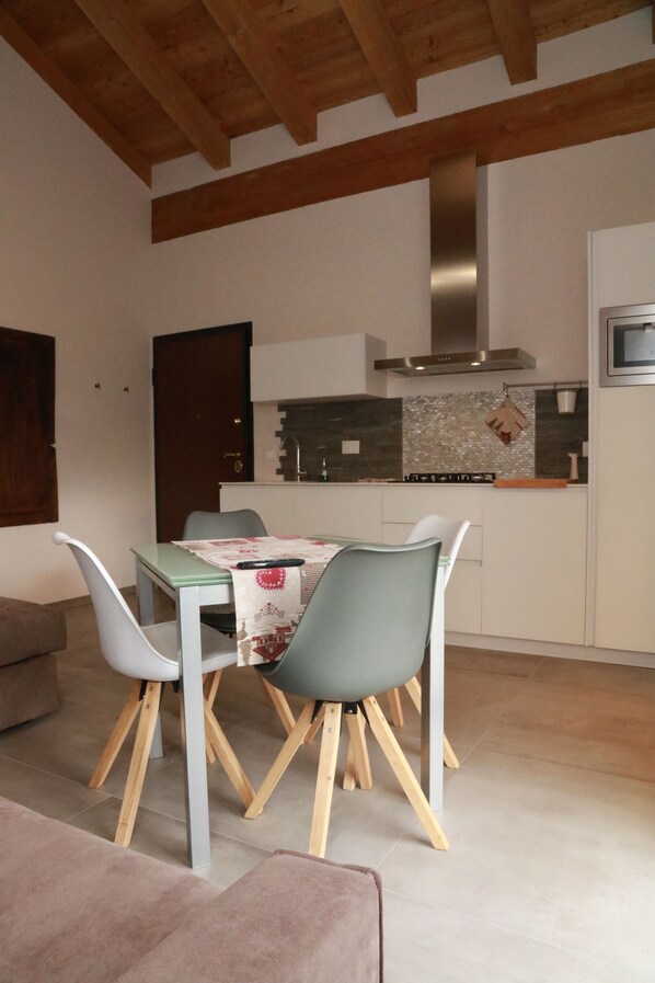 A modern kitchen with white cabinets, a stainless steel range hood, and a tiled backsplash. There is a dining area with a table and chairs. - The Harmony Of Nature (italia)