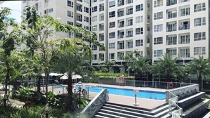 A swimming pool with steps leading down to it, surrounded by greenery and a multi-story building in the background. - Jolie Home - Sky Center - Block A (Ho Chi Minh City)