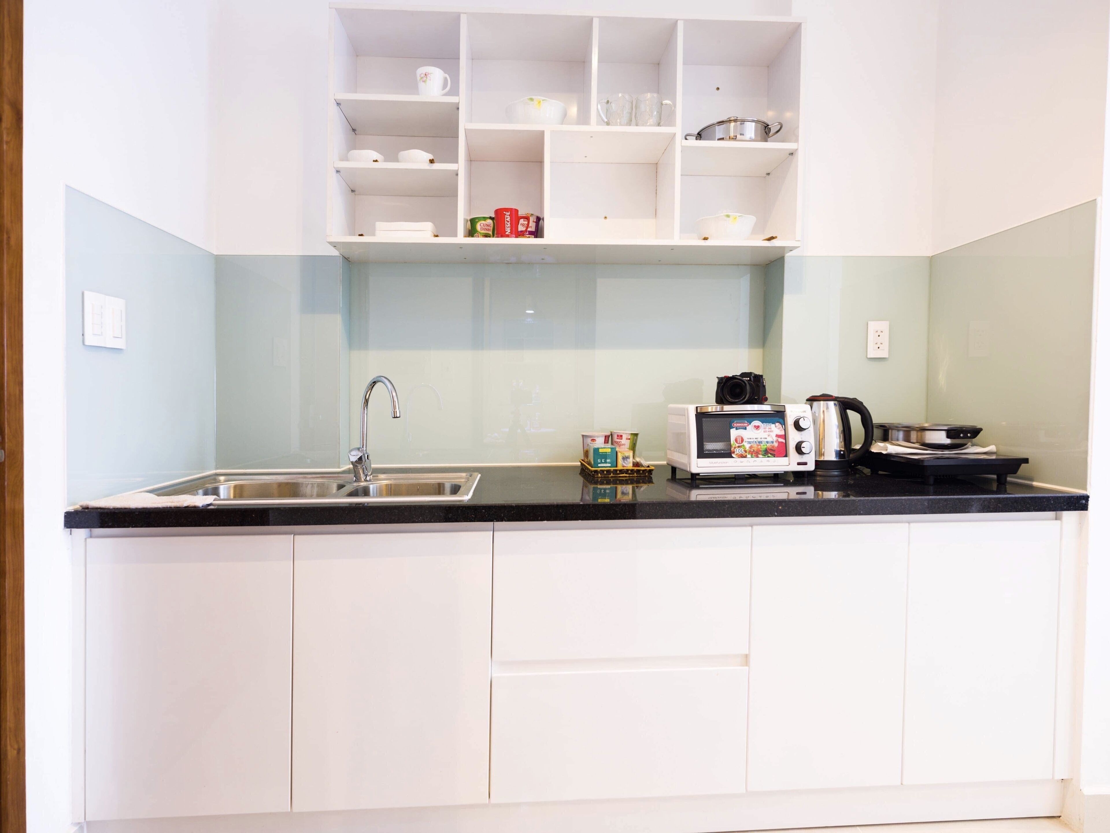 Una cocina con armarios blancos, encimera negra, microondas, hervidor y fregadero.