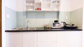 Una cocina con armarios blancos, encimera negra, microondas, hervidor y fregadero.