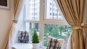 A room with a window, curtains, a plant, and decorative pillows. - Jolie Home - Sky Center - Block A (Ho Chi Minh City)