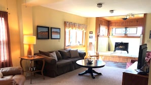 A cozy living room with a sofa, a coffee table, and a television. There is a fireplace and a window with curtains. - Lummis St. Bungalow located in the quaint township of Sodus Point NY! (Sodus Point)