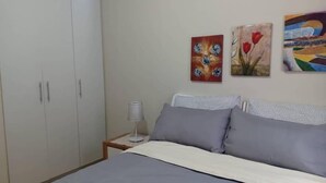Une chambre à coucher avec un lit, une literie grise, une table de chevet avec une lampe et trois tableaux accrochés au mur.