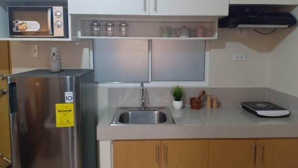 Une cuisine compacte équipée d’un réfrigérateur en acier inoxydable, d’un four à micro-ondes, d’un évier et d’un petit plan de travail sur lequel se trouvent une balance et une plante en pot.
