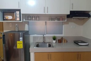 A compact kitchen with a stainless steel refrigerator, a microwave, a sink, and a small countertop area with a scale and a potted plant.