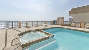 A pool with a view of the ocean, surrounded by a fence and lounge chairs.