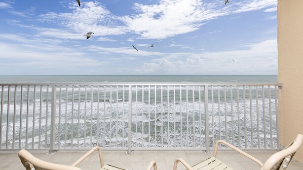 A balcony with a view of the ocean, featuring a railing and a few chairs.