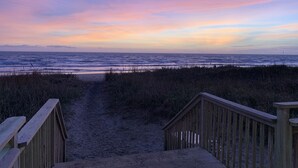 A wooden boardwalk leading to a beach with a view of the ocean and a sunset sky.