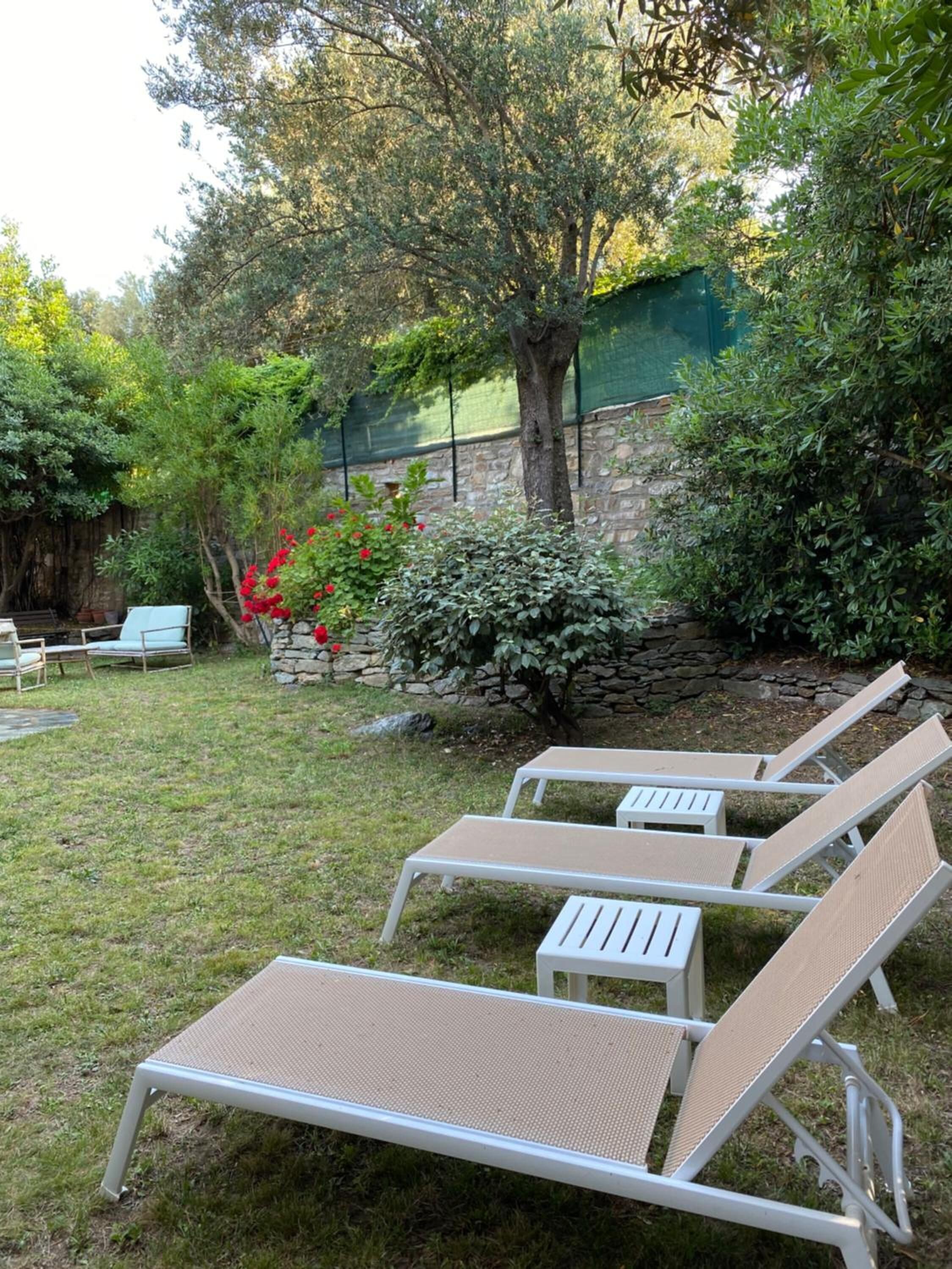 A garden with three white lounge chairs and a stone wall.