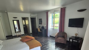 Una habitación de hotel con cama, escritorio, silla, televisor y ventana con cortinas.