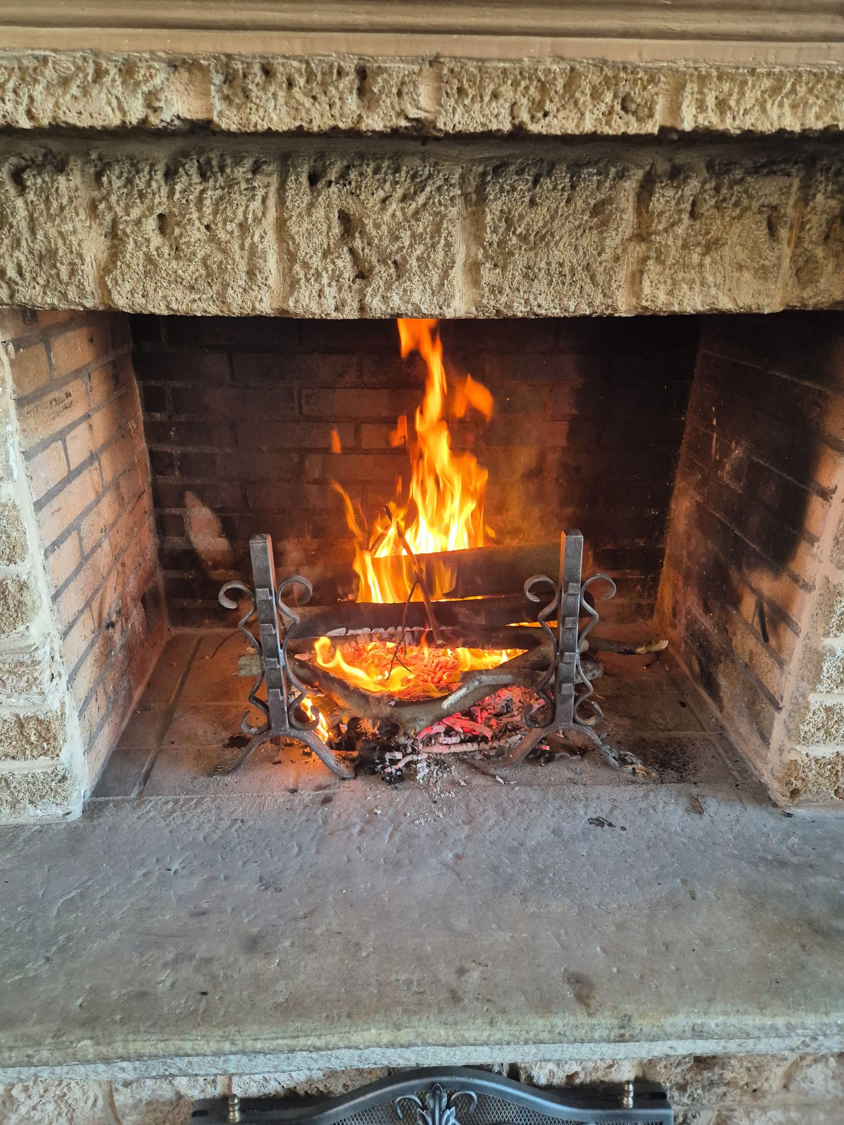 A fireplace with a fire burning inside, surrounded by brick walls.