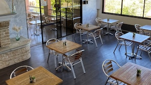 Un amplio comedor interior con varias mesas y sillas, grandes ventanales arqueados y vistas al exterior.