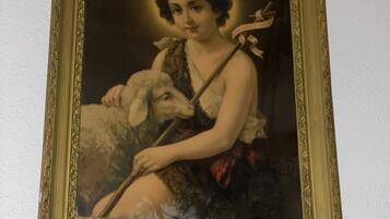 A framed painting of a woman with a lamb, set against a plain wall.
