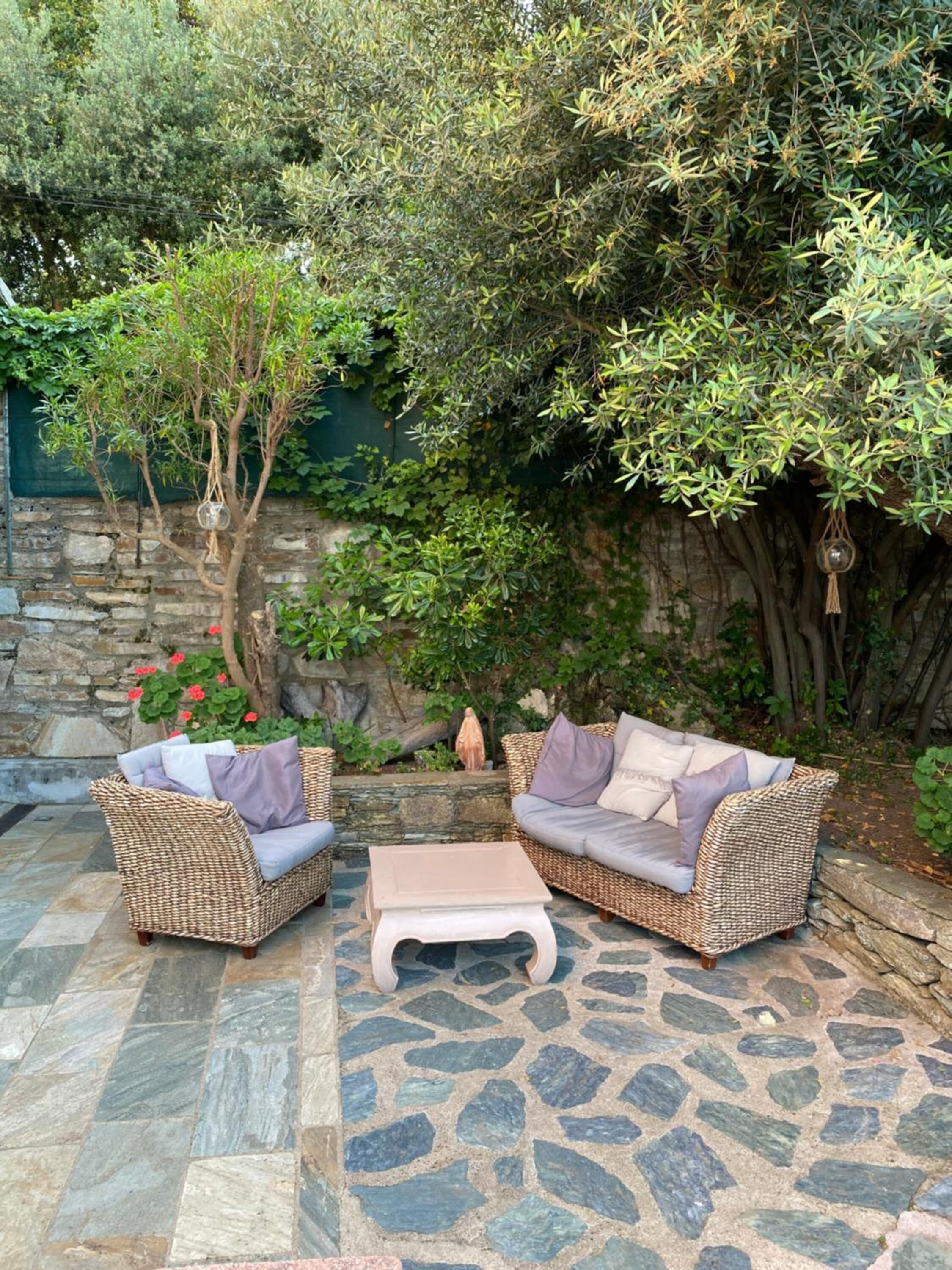 A patio area with wicker furniture, a stone floor, and a stone wall with greenery.