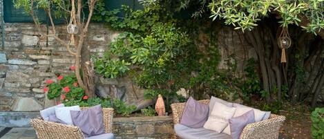 A patio area with wicker furniture, a stone floor, and a stone wall with greenery.