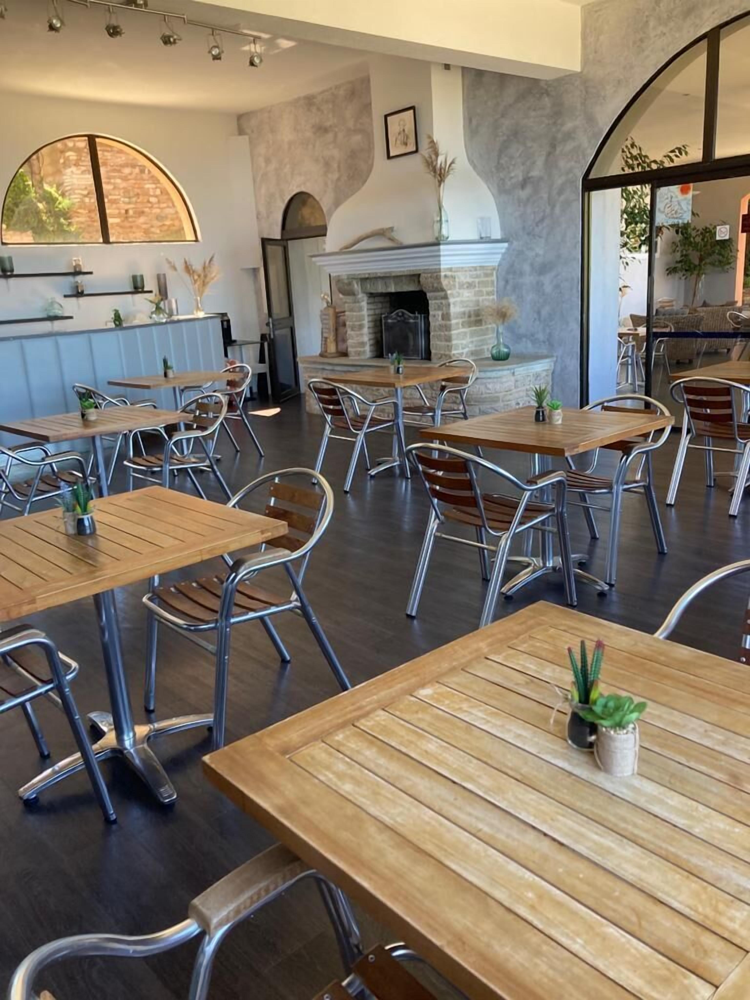 Interior de restaurante con mesas de madera y sillas de metal, chimenea de piedra y vistas al exterior.